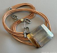 Full view of the necklace laid flat showing rectangular pendant and multiple leather cords.