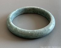 Photo of the natural light green jade bangle from a top-down angle on a neutral background.