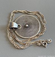 Photo of the necklace with the pendant laid flat, showing the circular pendant and twisted rope chain.