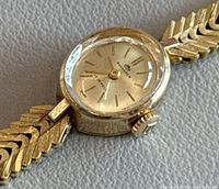 Close-up of the watch face showing gold tone dial with 17 jewels and Swiss marking, gold hands, and textured faceted crystal.