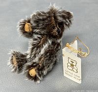Close-up image of the small gray and white teddy bear with tags attached, showing fur details and printed paw pads.