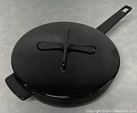 Photo of top view of black enameled cast iron skillet with lid closed showing the large cross-shaped handle on lid and side handle of skillet.
