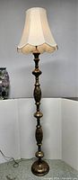 Full view of the vintage Persian style floor lamp with painted and brass inlaid details and scalloped fabric lampshade lit up.