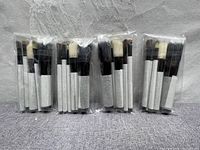 Four sealed sets of MAC makeup brushes, each containing a variety of brush shapes and sizes with white handles and black bristles, displayed on a grey cloth background.