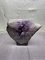 Front view of an amethyst cluster crystal cathedral with purple translucent crystals and rough basalt outer surface