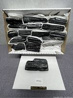 Box containing about 12 black tourmaline mineral stones nicely arranged on a white folded pad, each with characteristic glossy ridged texture.