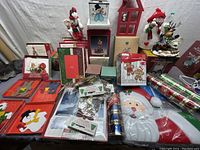 Wide view showing Santa, snowman, reindeer figures, several greeting cards, gift wrap rolls, and assorted decorations spread on table