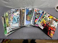 Photo showing a fanned display of multiple comic books including Marvel's Exiles and other titles, placed on a grey surface.