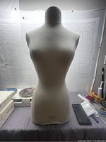 Front view of small female mannequin torso covered in cream fabric with a smooth head and no arms or stand.