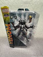 Front view of the sealed Marvel Select Venom 7-inch action figure in packaging showing figure and accessories inside clear plastic.