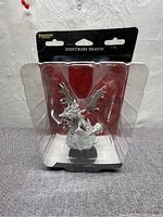 Front view of the sealed plastic clamshell package containing the unpainted Nightmare Dragon miniature, showing the product name and brand on packaging.