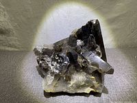 Main photo showing detailed close-up of the smokey quartz cluster's crystal points and structure under direct light, highlighting the smoky coloration and natural formation.