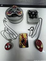 Photo shows two Spider-Man themed metal fidget spinners, one lighter with Spider-Man image, and two Spider-Man watch necklaces on white background.