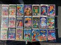 Full layout of 22 Walt Disney VHS movies on a dark surface showing full front covers.