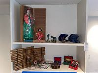 Shelf view showing dolls, brass bells, blue glass art tree, decorative boxes, and bamboo placemats