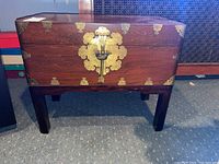 Full front view of wooden chest on stand with brass hardware and lock mechanism visible.
