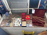 Full assortment of trays with earrings, brooches, ring, faux pearls and wooden jewelry box with label displayed on radiator cover