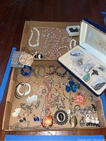 Overview shot of assorted jewelry in cardboard tray including necklaces, bracelets, earrings, brooches, jewelry box and cigarette case