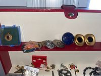 Photo of the jewelry box interior showing assorted pendants, earrings, pins, and gold-tone clip-on earrings.