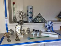 Overview of all items showing various brass bird figurines, glass bird figurines, porcelain vase, glass triangular prism object, porcelain duck figurine, wire tree sculpture, and a tall porcelain vase with floral designs.