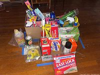 Photo showing assorted household cleaning and storage supplies including plastic bags, foil, and cleaning sprays grouped in open boxes.