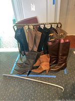 Front and side views of five pairs of ladies boots hanging on gold-tone metal boot rack. Varied colors including black, beige, and tan.