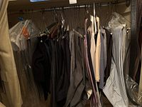 Hanging men's pants and shirts in various neutral and muted colors, showing the quantity and range of clothing in the lot.