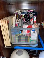 Metal mesh basket filled with various office supplies, folder edges visible on the left, and clipboard behind the basket.
