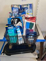 Photo showing a variety of oral care products in a black wire basket on a blue platform, including Oral-B Vitality electric toothbrushes, Glide dental floss, and CVS toothbrush covers.