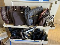 Photo of a white two-tier stand with multiple purses of various colors including brown fabric, black leather with studs, shiny metallic small purse, and maroon and brown leather purses.