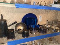 Full set of silver plated pitchers, bowls and plates on glass shelf with blue tape