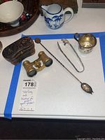 Photo of all lot items on table including mother of pearl opera glasses, leather case, sterling silver cup, spoon and tongs
