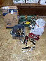 Full lot overview showing toilet seat box, gray plastic bin with tools, green toolbox, extension cords, paperwork and tape on floor.