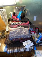 Overview photo of multiple winter scarves, gloves, and umbrellas arranged on a table with a lamp, showing different textures, colors, and patterns.