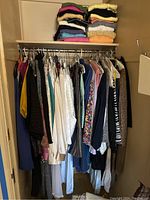 Wide view of women's clothes on hangers and stacked sweaters on shelf