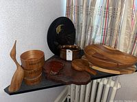 Wide view of the lot showing wood salad bowl with utensils, stack of three faux wood snack bowls, wood bird figurine, wood cutting boards, and black platter with fish design.