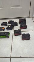 Photo showing 10 power tool batteries of various brands and sizes arranged on tiled floor.