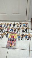 26 WCW wrestling action figures arranged in rows on a tiled floor with a 1999 WCW interactive microphone in unopened packaging.