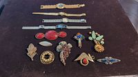 Full view of four watches and eight brooches laid out on dark surface.