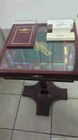 Mahogany-finished pedestal stand supporting glass-covered Monopoly game board