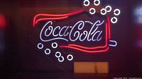 Front view of the rectangular LED Coca-Cola sign illuminated with red and white lights showing the logo and bubbles.