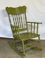Green antique-style solid wood rocking chair with detailed carvings on backrest and seat supports, spindled armrests and legs, shown from angle and front view.