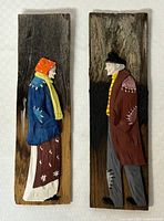 Show front view of both carvings on weathered cedar shingles, depicting a woman and a man in traditional clothing.