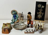 Wide view of entire lot showing all figurines, pottery, carved wood, and framed dried flower artwork