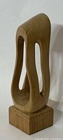 Front left angle view of the tall abstract wood carving on a rectangular base showing smooth curves and open voids.