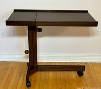 Wooden overbed table full side view showing the split top surface and swivel caster wheels.