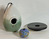 Overview of the pottery collection showing drop-shaped birdhouse, blue studio porcelain vase, and flower arranging frog on white background