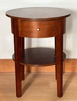 Front view of round wood side table showing drawer, shelf, and legs.
