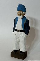 Full view of the wood carving figurine showing the front pose with blue hat, vest, white pants, and beard.