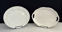 Two white platters displayed on stands: Italian oval with grapevine detail on left, Japanese oval with handles on right, on white surface with black background